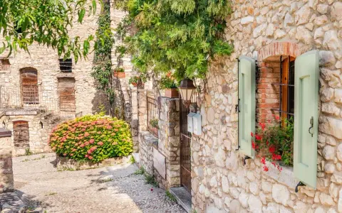 Un vicolo pittoresco tra i paesi del lago di Garda sponda veronese, con case in pietra, fiori e persiane verdi.