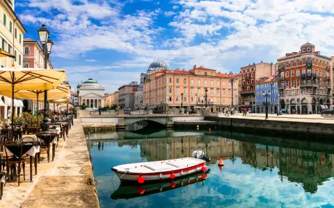 Un'incantevole vista di Trieste: un canale con una barca, caffè all'aperto e palazzi storici. Ecco cosa vedere a Trieste per un'esperienza indimenticabile.