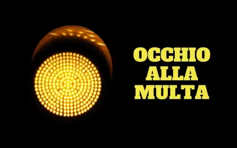 Semaforo giallo acceso, con la scritta "OCCHIO ALLA MULTA". Attenzione a non passare con il giallo, potresti ricevere una multa!