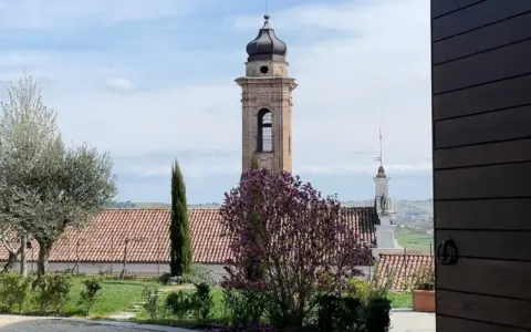 Torre campanaria e un albero in fiore, scorcio di un borgo tra le colline. Castagnole delle Lanze cosa vedere: un paesaggio incantevole.