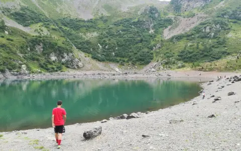Ragazzo in maglietta rossa ammira il **lago di Erdemolo**, circondato da verdi pendii montuosi e rocce.