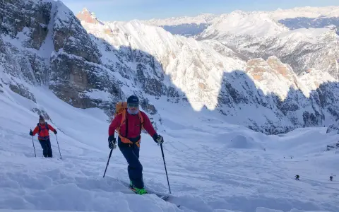 Sciatori scendono da un ripido pendio innevato sul Monte Cristallo, con vette maestose sullo sfondo. La **funivia** è lontana, ma l'avventura è appena iniziata.
