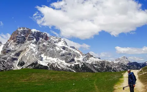 Un uomo con bastoncini da trekking su un sentiero in Trentino, con imponenti montagne innevate sullo sfondo. Un'esperienza di trekking trentino facile e panoramica.