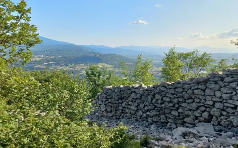 Muro di pietra a secco con vista panoramica su una valle alpina e montagne all'orizzonte.