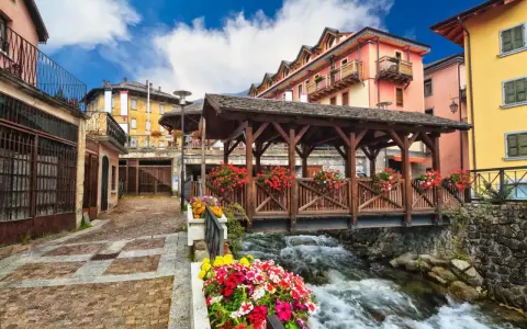 Un pittoresco ponte di legno coperto, adornato di fiori, attraversa un torrente impetuoso. Un incantevole scorcio di cosa vedere in un borgo alpino.