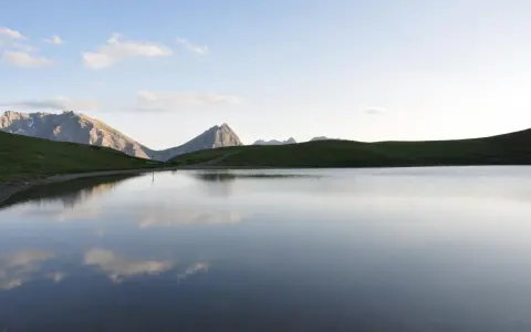 Sestriere estate: un lago alpino riflette le montagne e il cielo azzurro, un'oasi di pace.