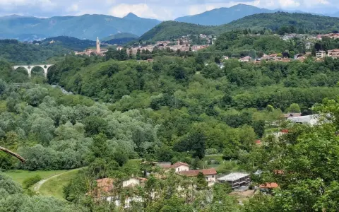 Panoramica collinare con un ponte ad archi, un campanile e case sparse a Cassano Magnago, circondata da rigogliosa vegetazione.