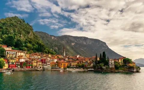 Colorate case affacciate sul lago di Lecco, con montagne verdi sullo sfondo e un cielo nuvoloso.
