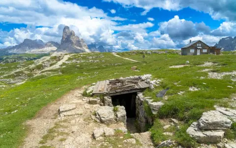 Un sentiero conduce a un rifugio di guerra sul Monte Piana, con le maestose Tre Cime di Lavaredo sullo sfondo.