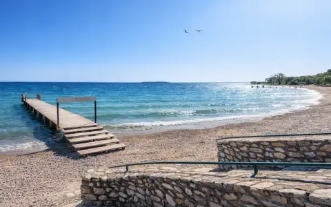Molo in legno sul **Manerba del Garda strand**, con acqua cristallina e cielo azzurro. Due gabbiani volano sopra il lago.