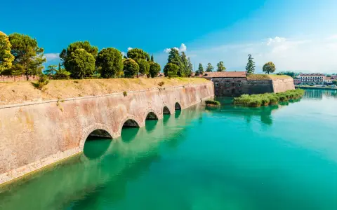 Fortificazioni storiche con archi in mattoni e acqua turchese, dove si trova Peschiera del Garda.