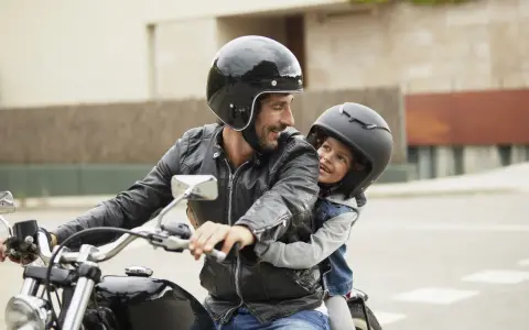 Padre e figlio sorridono in moto, rispettando il nuovo codice della strada per bambini in moto.
