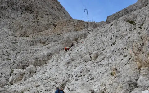 Escursionisti affrontano la **difficoltà** del sentiero verso il **Rifugio Re Alberto**, aggrappandosi a cavi d'acciaio su un ripido pendio roccioso.