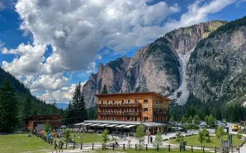 Edificio in legno a Pederu San Vigilio, con montagne imponenti e cielo nuvoloso.