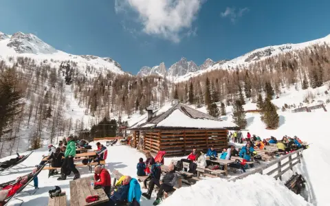 Malga Valcigolera, un rifugio alpino innevato con gente seduta ai tavoli. Per sapere come arrivare, guarda l'immagine.