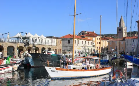 Porto di Muggia cosa vedere: barche a vela, edifici storici e un campanile svettano sotto il cielo azzurro.