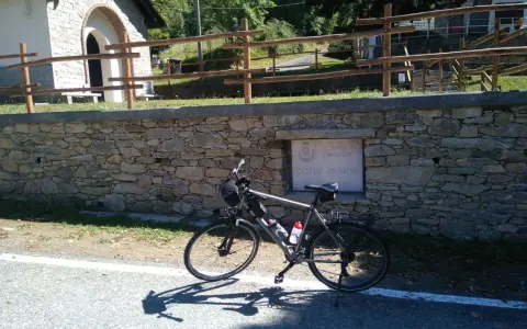 Bicicletta ferma sul ciglio della strada, con un muretto in pietra e un cartello che indica "Colle Braida".