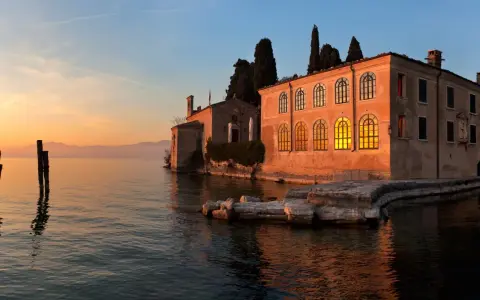 Punta San Vigilio: un tramonto dorato illumina la spiaggia e l'antica villa affacciata sul lago.