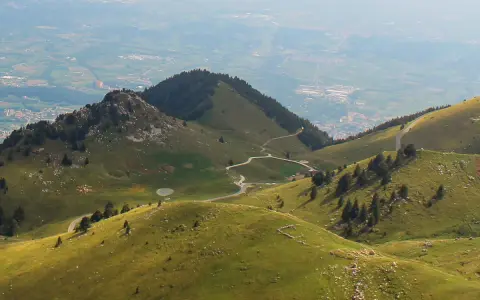 Panorami verdi con strade tortuose e malghe sul Monte Grappa. Un gregge pascola vicino a un piccolo lago.