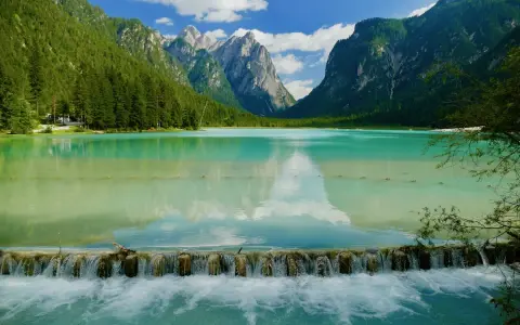 Splendido lago turchese incastonato tra montagne verdi, ideale per una toblacher see wanderung. Una cascata artificiale crea un effetto scenografico.