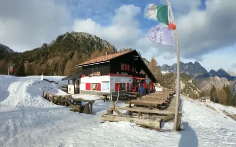 Rifugio Antelao innevato, con tavoli esterni e bandiere. Informazioni su come arrivare al rifugio sono visibili.