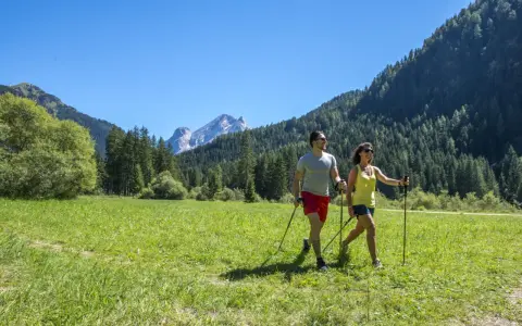 Coppia fa nordic walking in un prato verde con montagne sullo sfondo, ideale per canazei escursioni facili.