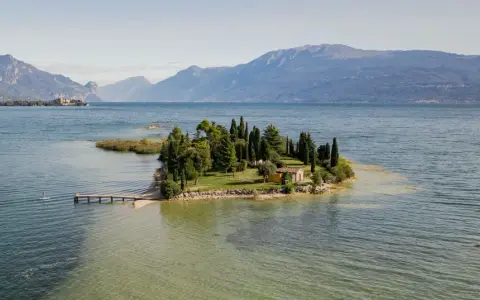 Un'incantevole isola dei conigli sul Lago di Garda, con un piccolo molo e una casetta gialla tra i cipressi.