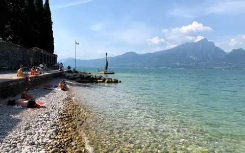 Persone rilassate sulla torri del benaco spiaggia, con acque limpide e montagne sullo sfondo.