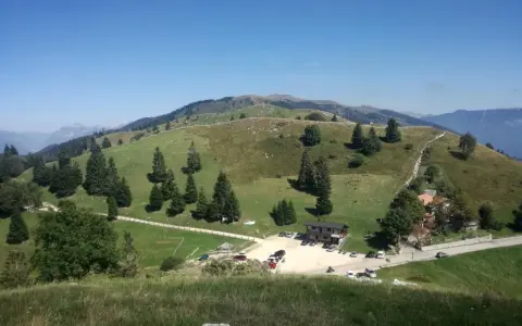 Panorami verdi e dolci colline del Pian delle Femene, con un rifugio e parcheggio.