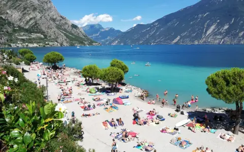 Una vivace spiaggia di Limone sul Garda, con gente che prende il sole e nuota nelle acque turchesi del lago.