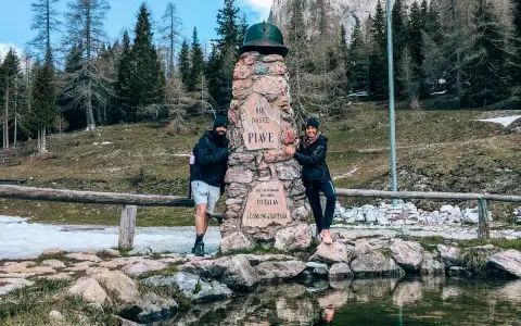 Coppia sorridente vicino a un monumento in pietra a Sappada, ideale per passeggiate facili.