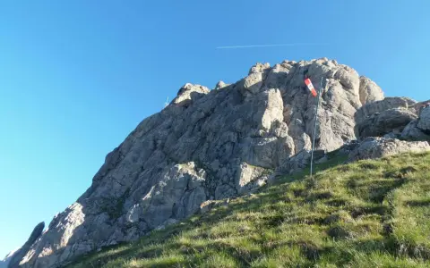 Vetta rocciosa con bandiera segnavento. Per col rodella come arrivare, segui il sentiero erboso verso la cima.