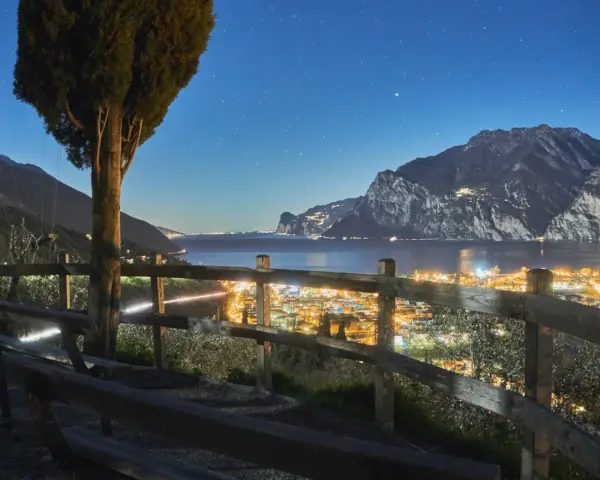 Peschiera del Garda di sera: un panorama mozzafiato con luci scintillanti, montagne imponenti e un cielo stellato. Ideale per una serata romantica.