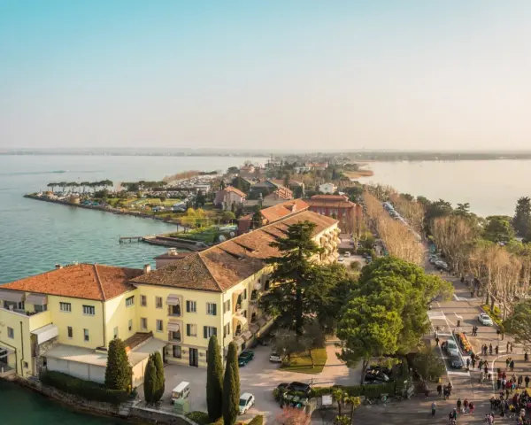 Vista aerea del centro storico di Sirmione, con edifici storici, lago e passeggiata affollata.