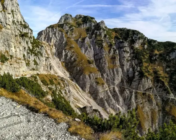 Sentiero roccioso in montagna, parte della strada degli eroi anello, con vegetazione sparsa e cielo azzurro.