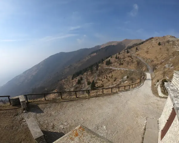 Strada tortuosa sul Monte Palon, Grappa, con vista panoramica sulle montagne e cielo azzurro.