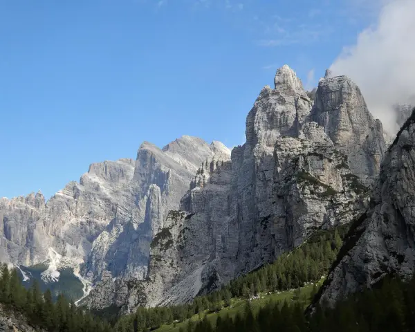 Imponenti cime rocciose dei monti di Framont si stagliano contro un cielo azzurro, con foreste di conifere ai loro piedi.
