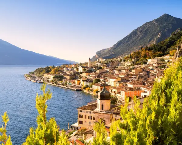Un perfetto weekend sul lago di Garda: borgo colorato affacciato sull'acqua blu, montagne verdi e cielo limpido.