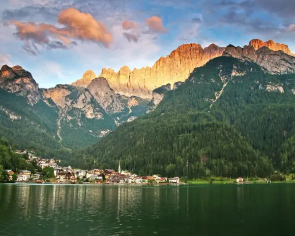 Un incantevole giro del lago di Alleghe, con il paese incastonato tra boschi e montagne maestose illuminate dal sole al tramonto.