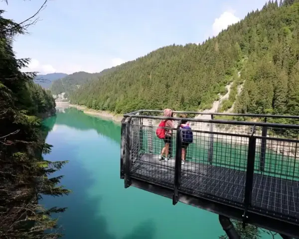Due persone su una piattaforma panoramica ammirano il lago di Val Noana. Ecco come arrivare a questo splendido lago alpino.