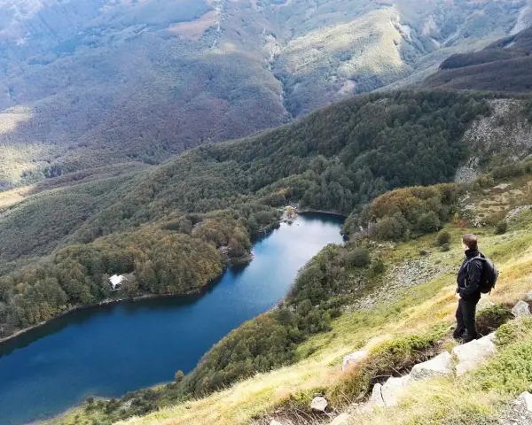 Un escursionista ammira il lago Santo Modenese, circondato da boschi autunnali e montagne.