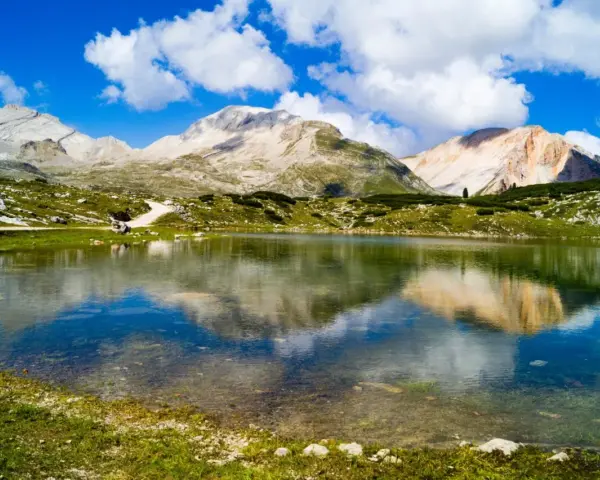 Un limpido lago di limo riflette montagne maestose e un cielo azzurro con nuvole bianche.