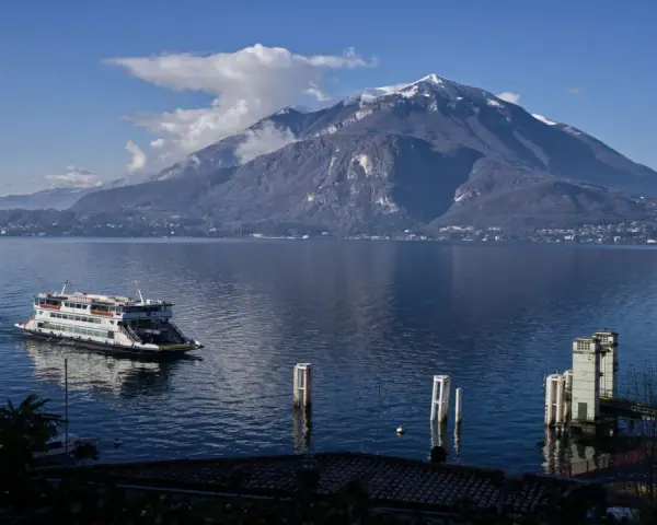 Traghetto sul lago di Como, con montagne innevate sullo sfondo e il pittoresco varenna centro storico.