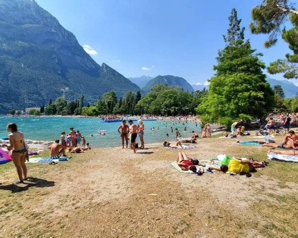 Spiaggia sabbioni Riva del Garda affollata di bagnanti sotto le montagne.