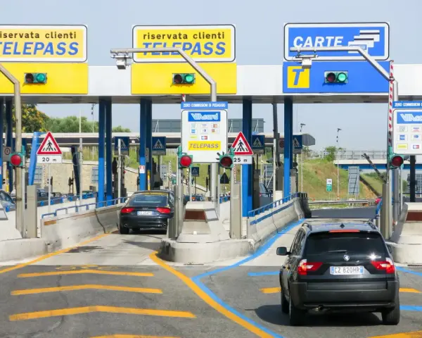 Casello autostradale con auto in coda. Segnaletica per Telepass e carte di credito. Possibile problema di mancato pagamento Telepass per un veicolo.