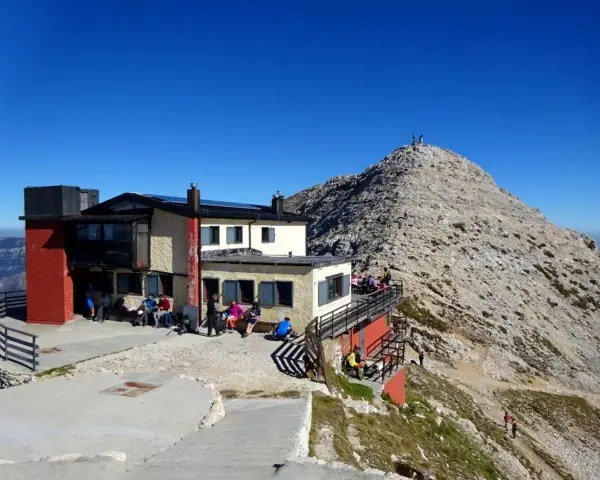 Rifugio Fraccaroli, un punto di ristoro in montagna. Per capire come arrivare, guarda la foto: un edificio con persone sedute all'esterno, con una vetta rocciosa sullo sfondo.