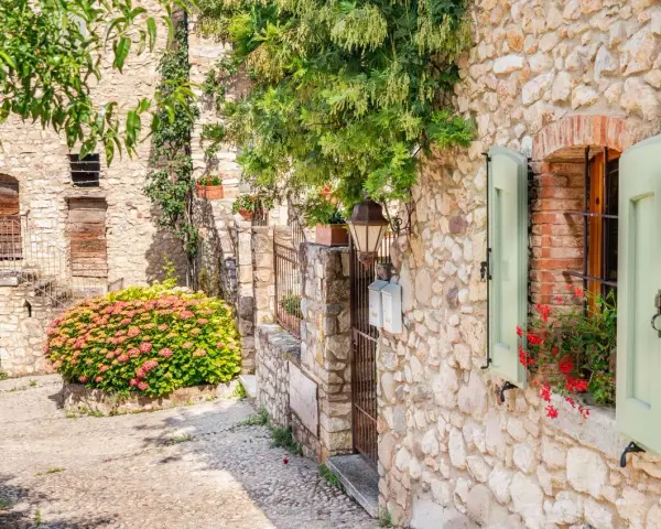 Un vicolo pittoresco tra i paesi del lago di Garda sponda veronese, con case in pietra, fiori e persiane verdi.
