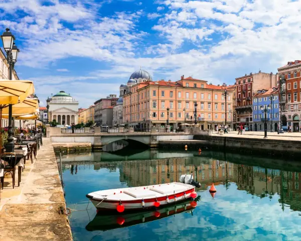 Un'incantevole vista di Trieste: un canale con una barca, caffè all'aperto e palazzi storici. Ecco cosa vedere a Trieste per un'esperienza indimenticabile.