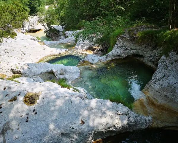 Acque cristalline scorrono tra le rocce levigate dei **cadini del Brenton**, creando piscine naturali immerse nel verde.