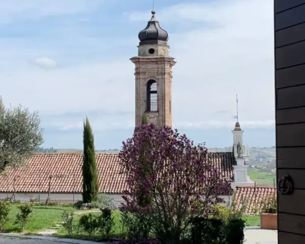 Torre campanaria e un albero in fiore, scorcio di un borgo tra le colline. Castagnole delle Lanze cosa vedere: un paesaggio incantevole.